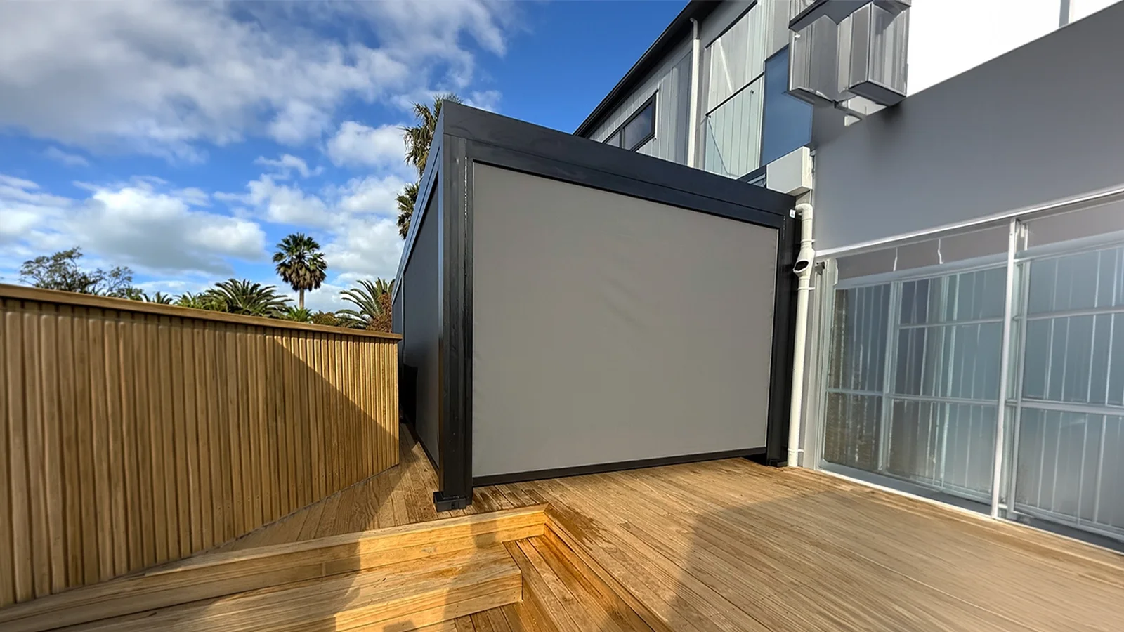 Automated motorized outdoor blinds stopping midway on a contemporary covered patio structure.
